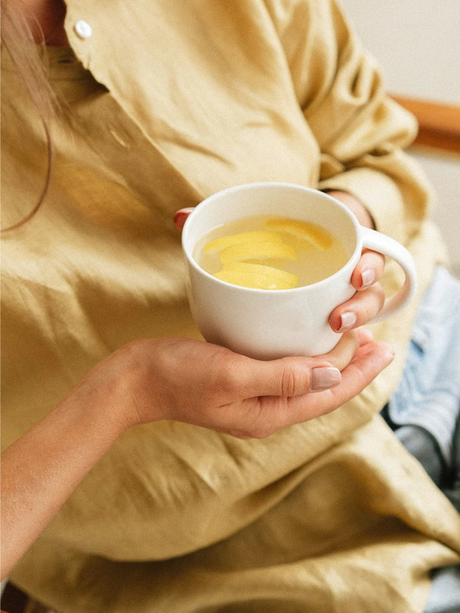 handcrafted stoneware mug. a white stoneware mug photographed in hands containing lemon water.