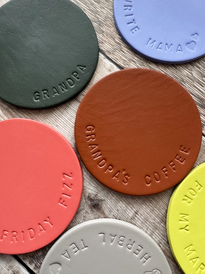 Handmade leather coasters in various colours, embossed with personalised messages like 'Grandpa's Coffee' and 'Favourite Mama.' Stylish and durable drink coasters, perfect for gifts and home decor