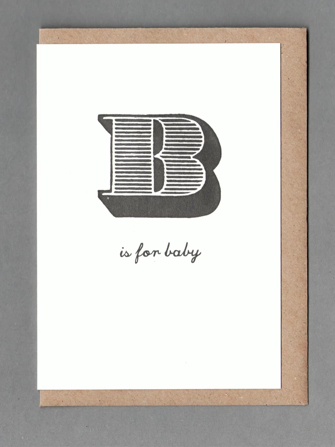 White card with black text reading 'B is for baby' with a kraft envelope behind it