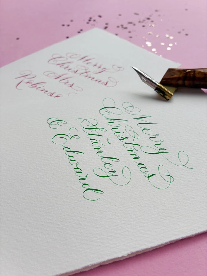 Close up of a calligraphy Christmas card in green ink, with a calligraphy pen on top