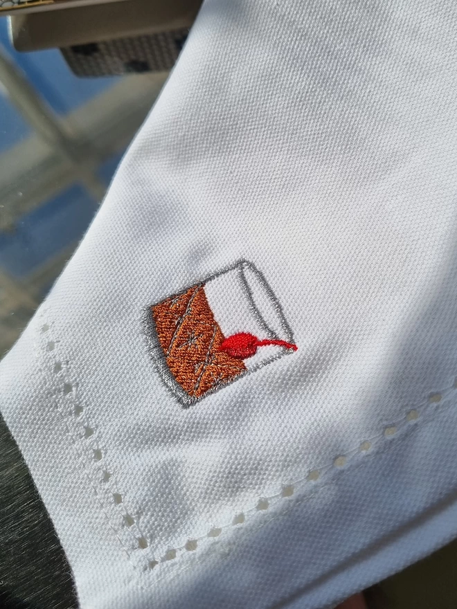 A close up of an embroidered old fashioned cocktail on a white napkin