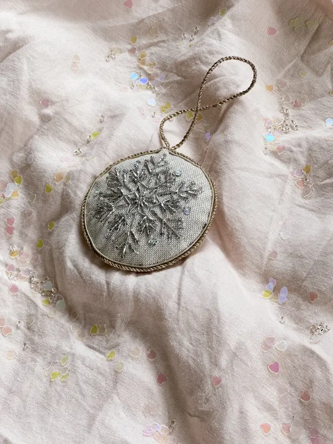 embroidered linen nutcracker snowflake decoration. beaded snowflake hanging ornament photographed on pale pink fabric background.