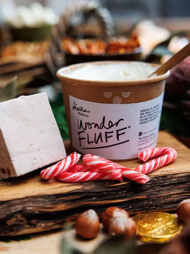 Vanilla Wonder Fluff Tub, the tub on a wooden table surrounded by lots more sweet treats. 