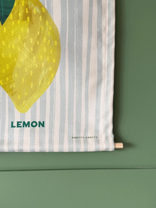 Cotton Lemon Wall Hanging, hanging on a green wall. 