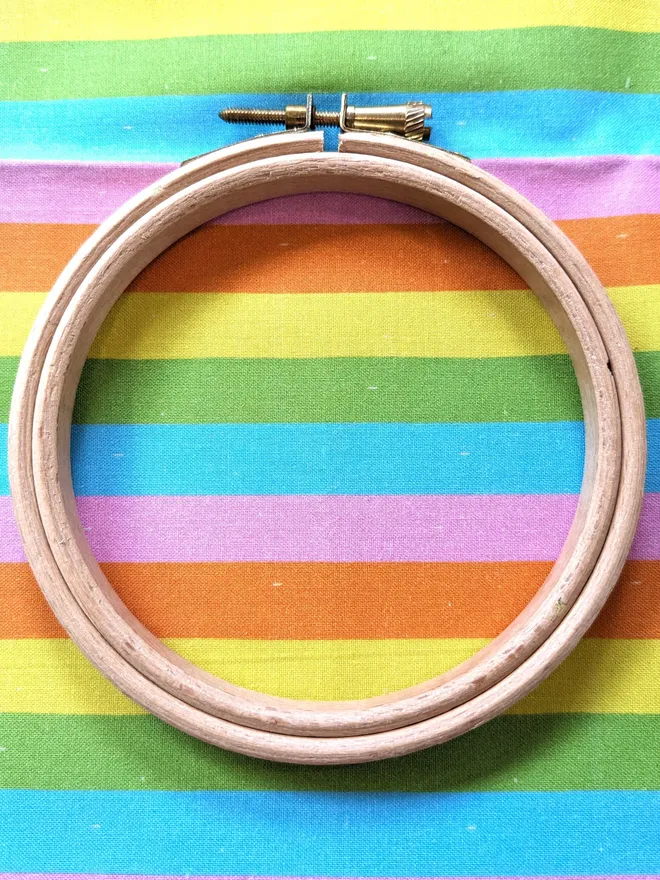 A wooden embroidery hoop lying on fabric with a colourful stripes design