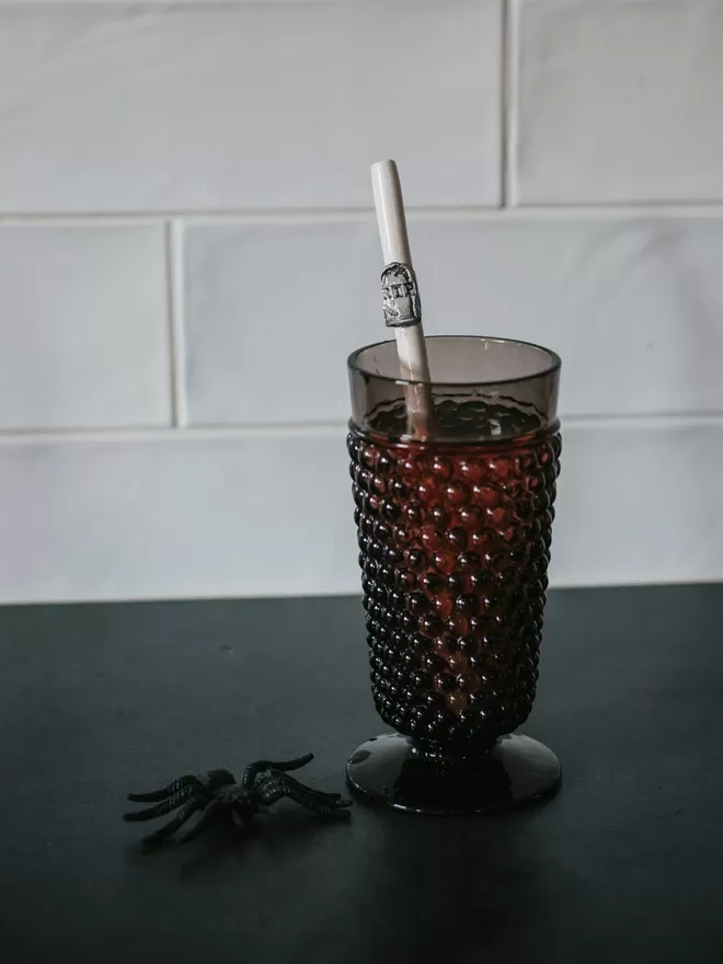 RIP ceramic Halloween straw by Bill and Ben seen in a black mug with a plastic spider next to it.