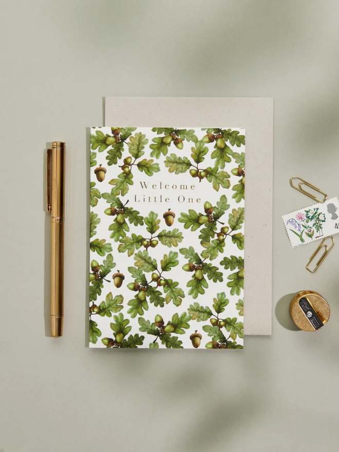 'welcome little one' illustrated oak leaf card. a white card illustrated with oak leaves photographed against a grey background.