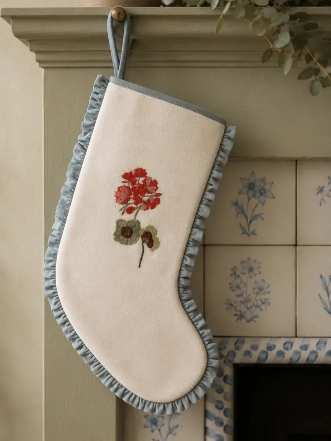 Geranium stocking on ivory wool with light blue linen frill. Styled on a sage green wooden fireplace with vintage blue and white floral tiles.