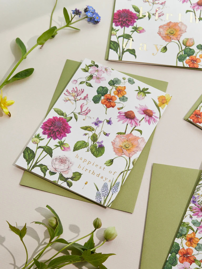 'Happiest Of Birthdays' Illustrated Floral Card. a white floral card and green envelope photographed against a plain background.