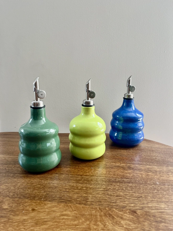 a collection of 3 colourful chubby oil bottles with wavy sides on a wooden table. forest green, lime green and cobalt blue 