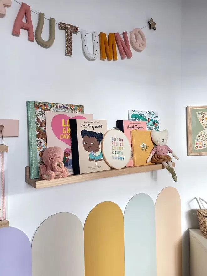 A gorgeous colourful kids room. A solid wood picture ledge shelf is styled up with kids books, teddies and children's decor.