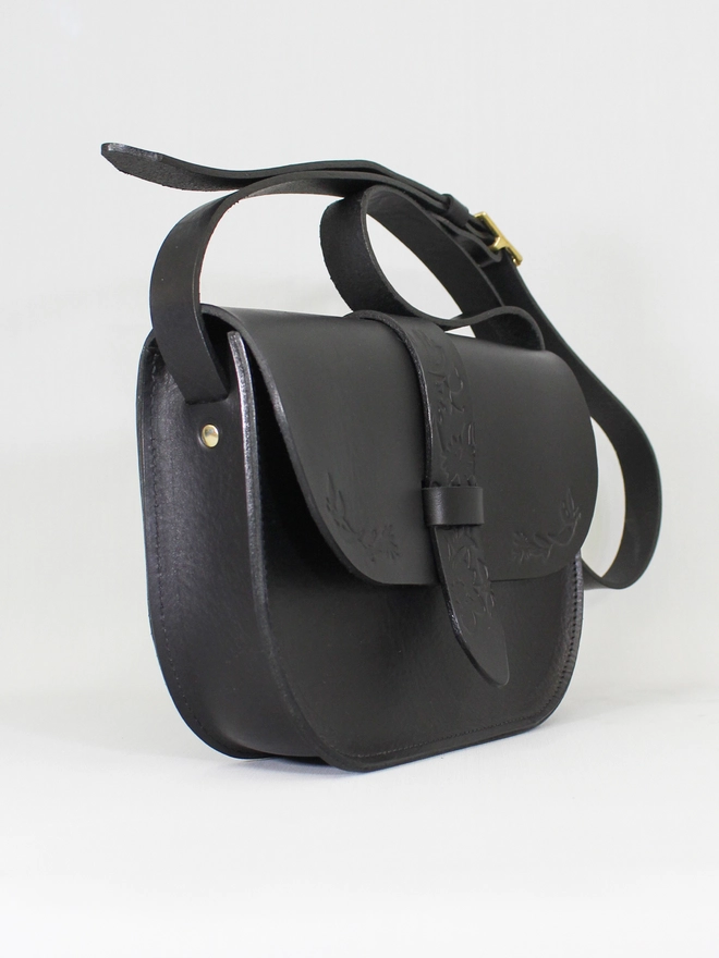 a side shot of a black vegetable tanned leather saddle bag with flower art embossed into the leather by Natthakur
