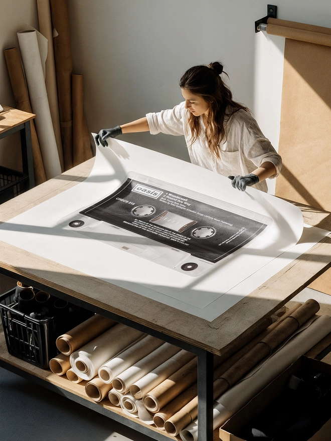 oasis wonderwall cassette tape print. artist unrolling print on studio desk.