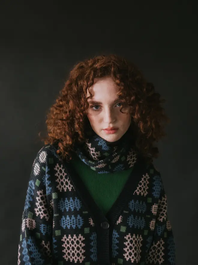 Model wearing pieces from MABLI's 'Carthen' collection, featuring the Carthen Wrap in the vibrant 'Emeralds' colour-way. The design showcases bold, colourful patterns inspired by traditional Welsh blanket tapestry.