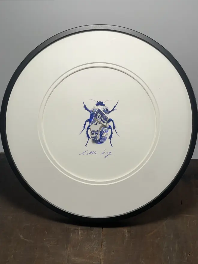Hand-drawn, painted, mosaic clay, blue vintage Chinese Willow Tree pottery insect on white double mounted card, in a black circular frame.