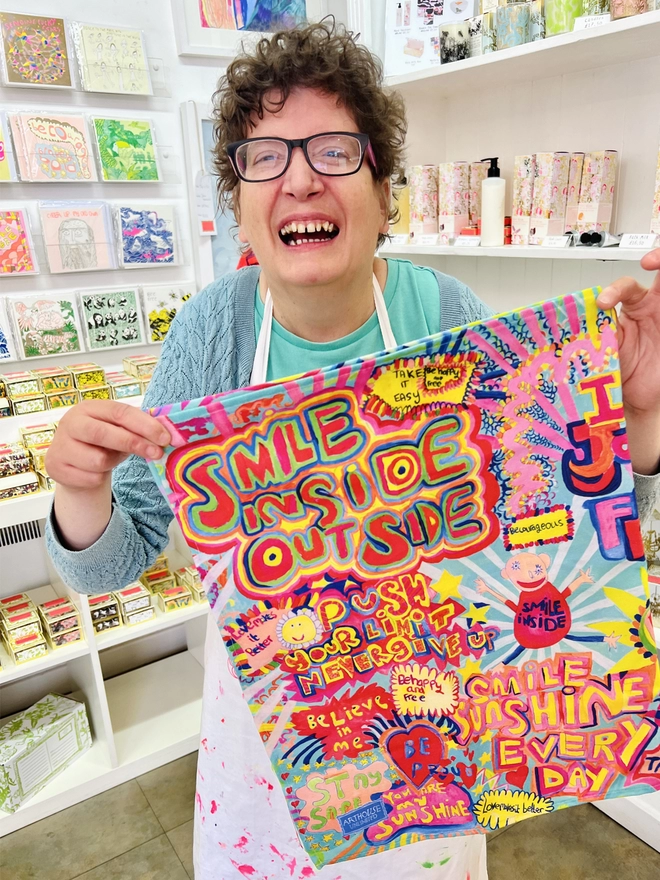 Happy artist holding full of joy 100% organic cotton charity tea towel with colourful positive messages