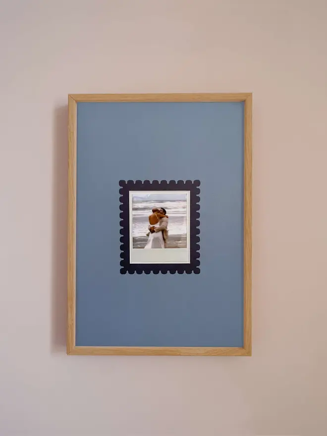 The Scallop Instax Square Mount frame with a blue mount featuring a decorative scallop border around a centered Instax Square photo, displayed on a neutral beige wall.