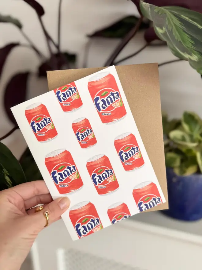 fanta cans illustrated card. card photographed with brown kraft envelope with houseplants in background.