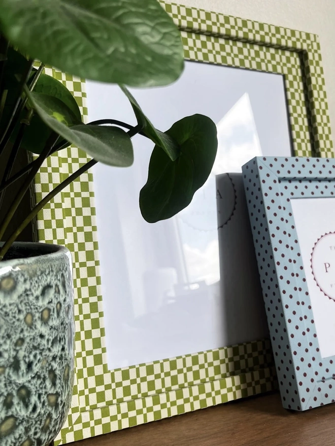 Green & Beige Checkered Frame, a colourful frame sitting on a wooden surface. It is joined by another colourful frame. 