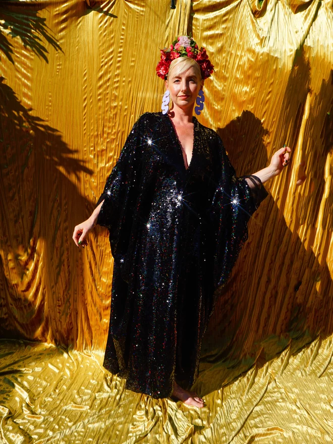 Petrol Black Holographic Sequin V-neck Kaftan Gown seen on a woman with her arms up wearing a flower headdress.