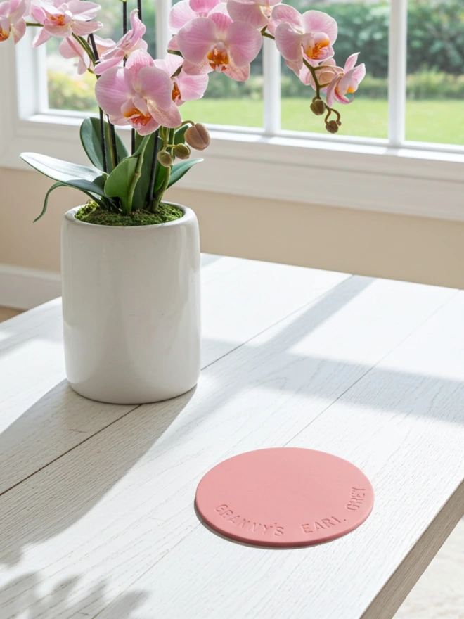 pink coaster with Grannys Earl Grey stamped on it with a vase of flowers on the table.