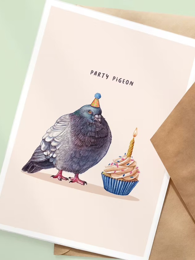 illustrated party pigeon birthday card. a pink card featuring a pigeon wearing a party hat with a birthday cupcake.