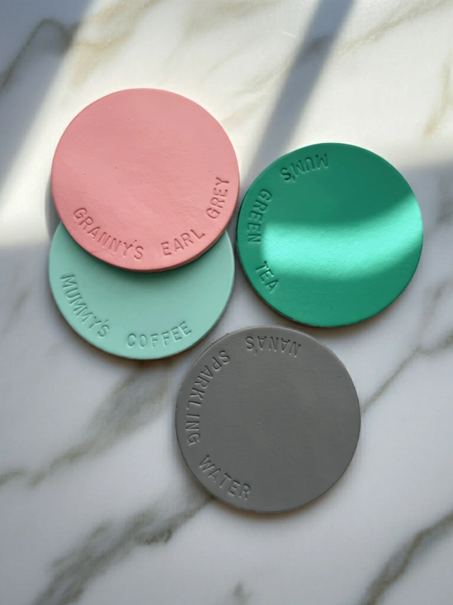 personalised brightly colour pastel coasters, in pale pink, mint green grey and seafoam.  Lying on a marble background.