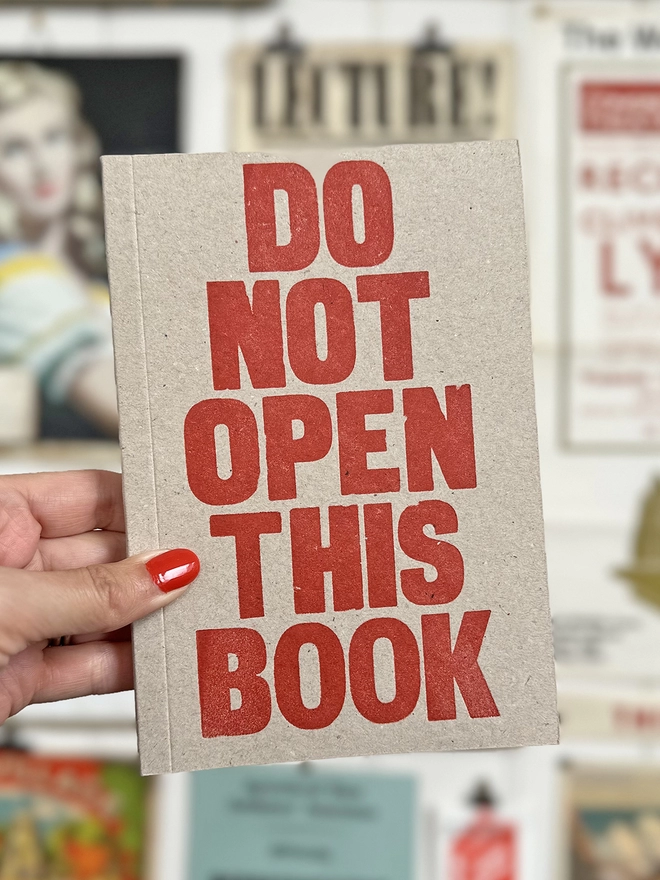 hand holding the letterpress notebook DO NOT OPEN THIS BOOK printed in red ink on a greyboard cover