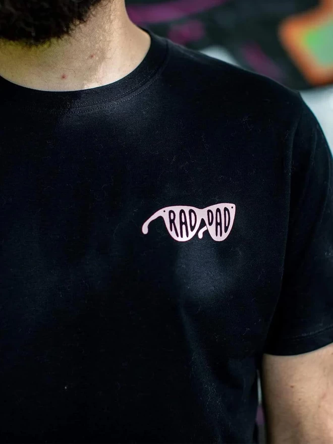 Close up of the Black & Beech black Rad Dad t-shirt with the words Rad Dad written in pink on the left breast