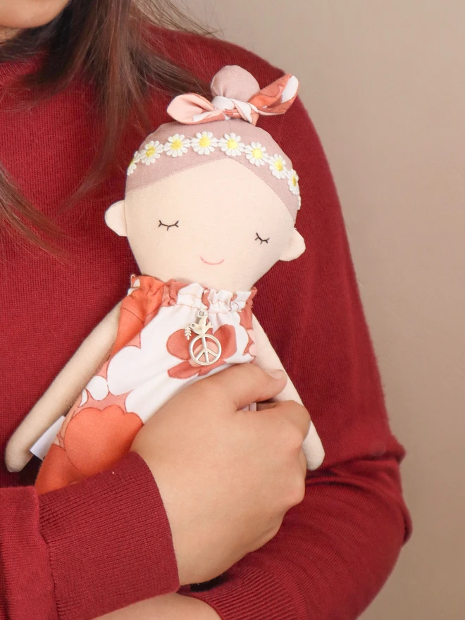 Handmade fabric doll called Peace Wishing Flower Child Doll, wearing peach and white retro floral dresses, daisy headbands, and bow topknots. It has serene embroidered face, peace sign charm around its neck