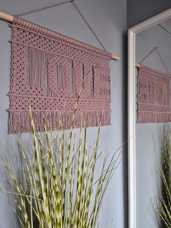 love macrame wall banner in pink cotton sitting on a wood dowel hanging on a wall celebrating love and connection to your space