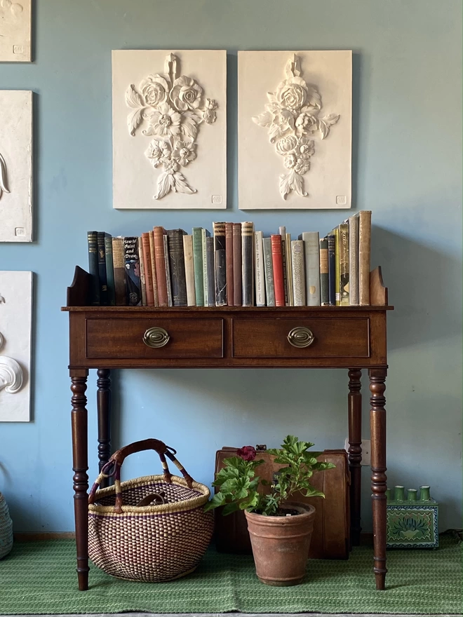 Two plaster bas-relief wall plaques with flower designs hanging above a table