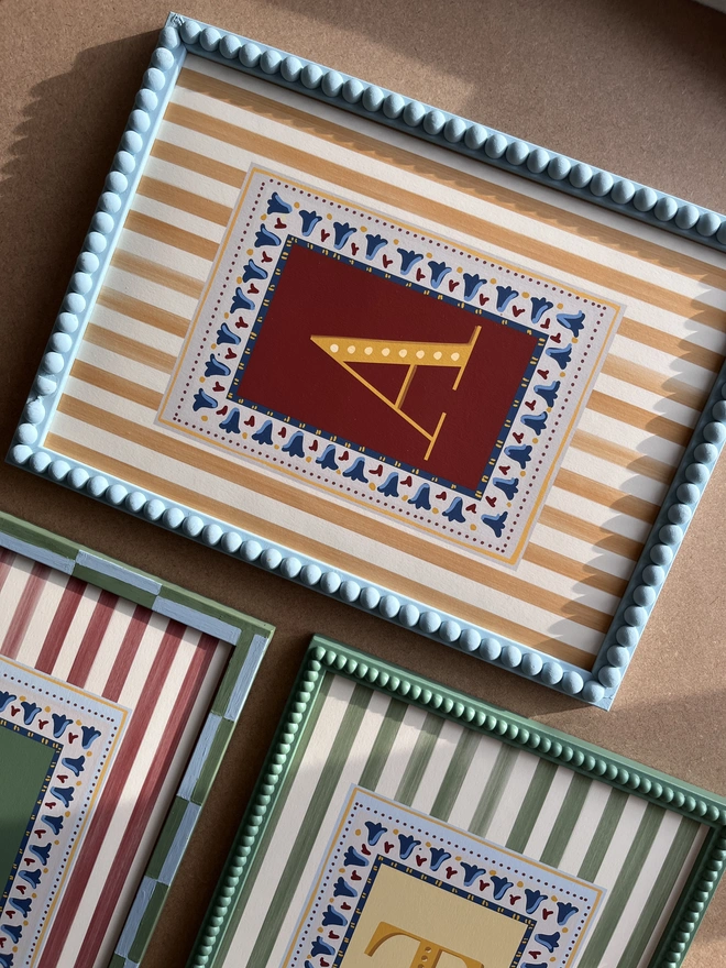 Close-up of Annabel Wond Interiors’ personalized stripy letter prints in custom-painted decorative frames, featuring hand-painted vertical stripes, colorful borders, and bold initials—ideal for children’s room and nursery wall art.
