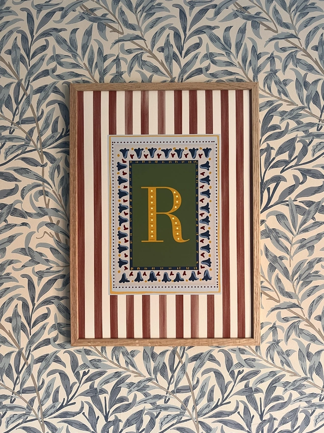 Elegant stripy letter print by Annabel Wond Interiors, featuring a bold green“R” with a decorative border on a red and white striped background, framed