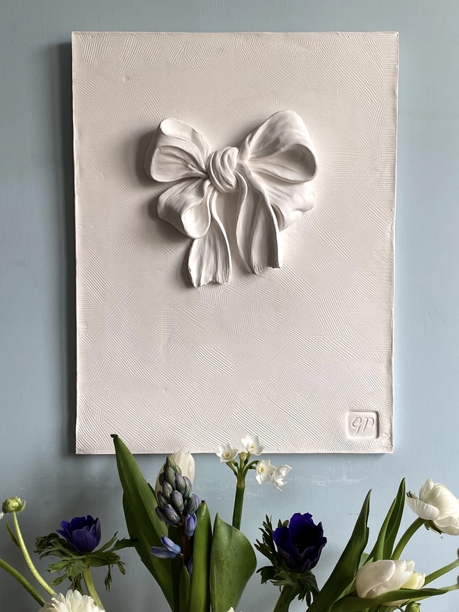 Plaster bas-relief wall plaque with bow and ribbon design with a vase of flowers underneath