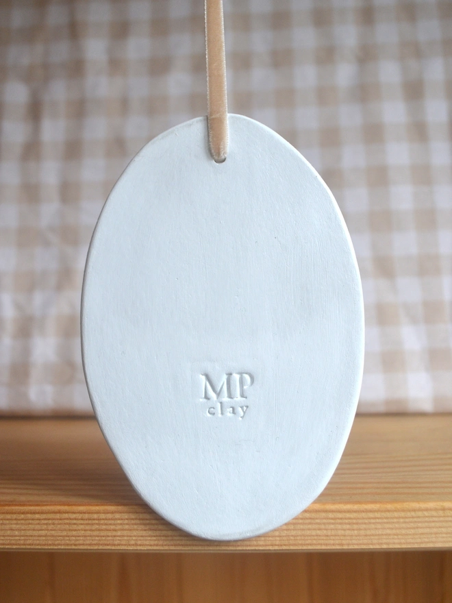 back of white oval ceramic decoration with 'MP' logo