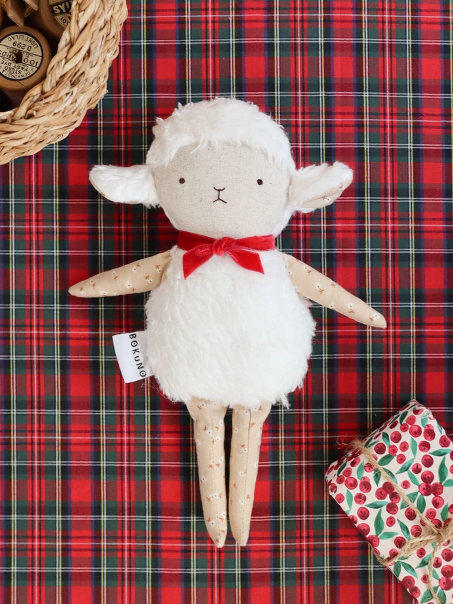 Handmade lamb doll with a fluffy white body, stitched face, beige floral fabric arms and legs, and a small red velvet bow tied around its neck.