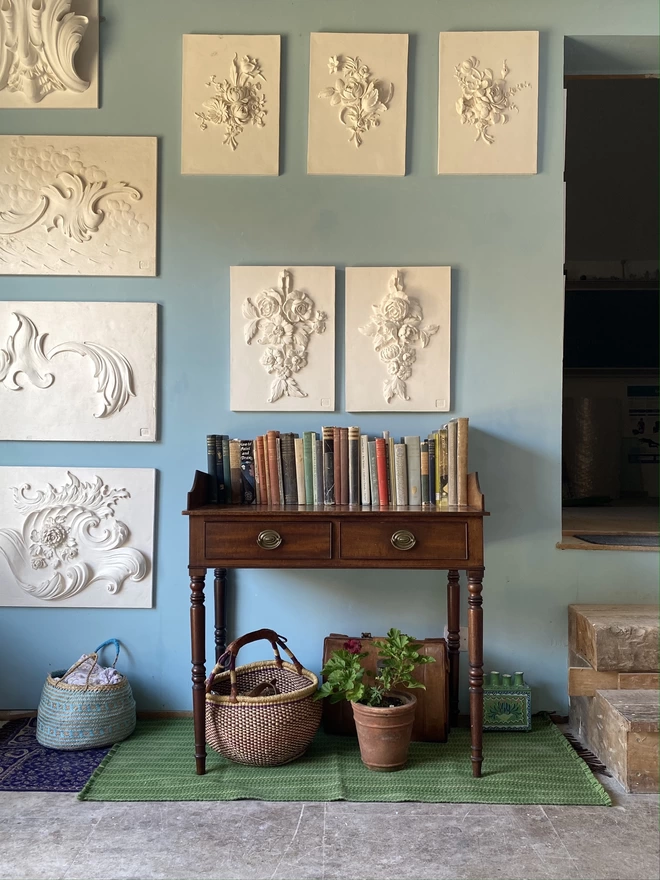 Gallery wall of sculptural wall plaques hanging above a table in the artists studio