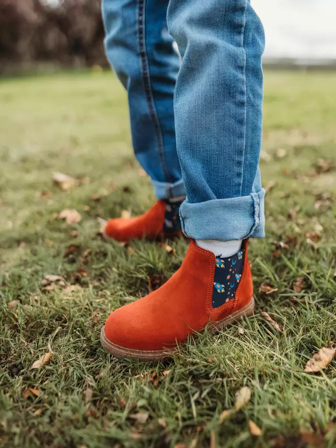 Child wearing red/ rust coloured suede chelsea boots with a space ship print