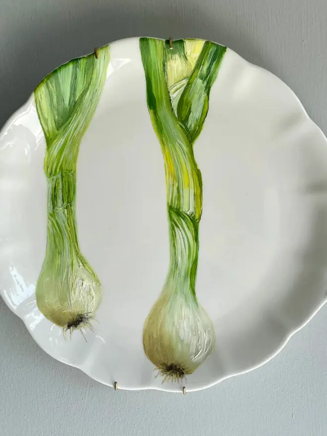 Oil Painted Large Spring Onions On Vintage Cake Plate, hanging on a grey wall. 