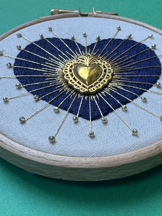 An embroidered heart in a hoop with gold beads and floss over the top