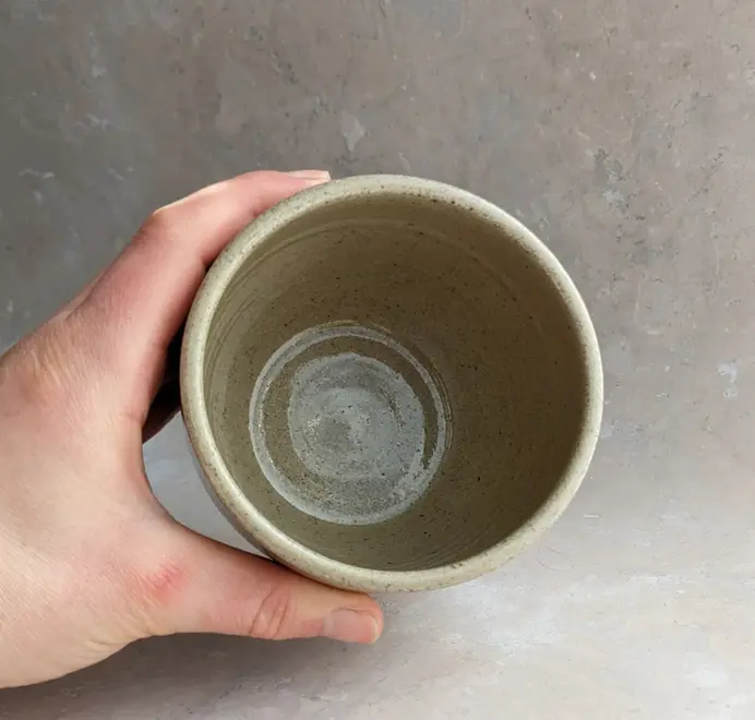 Birds eye view of biscuit coloured croissant coffee cup with a subtle croissant design, placed against a grey marble background.