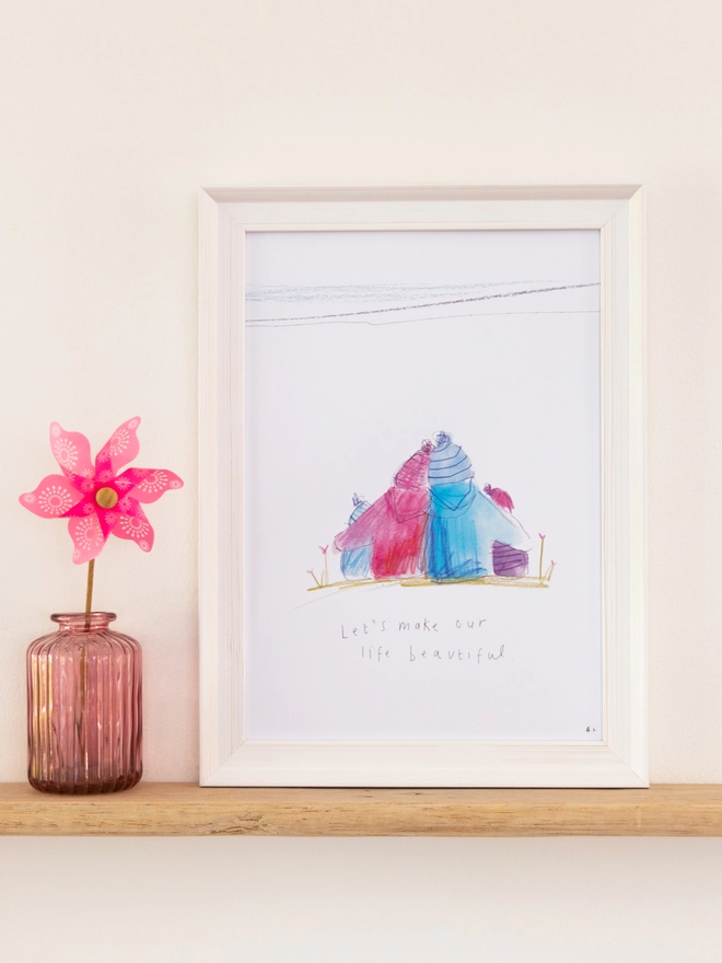 A sketchy muma print in a white frame next to a pink windmill in a vase