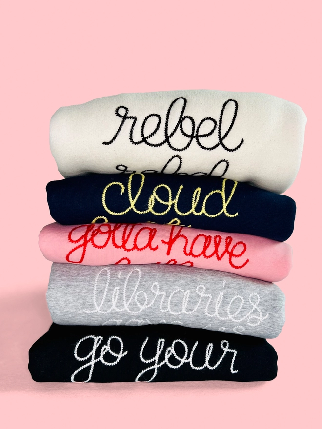 A colourful bundle of embroidered sweatshirts on a pink background 