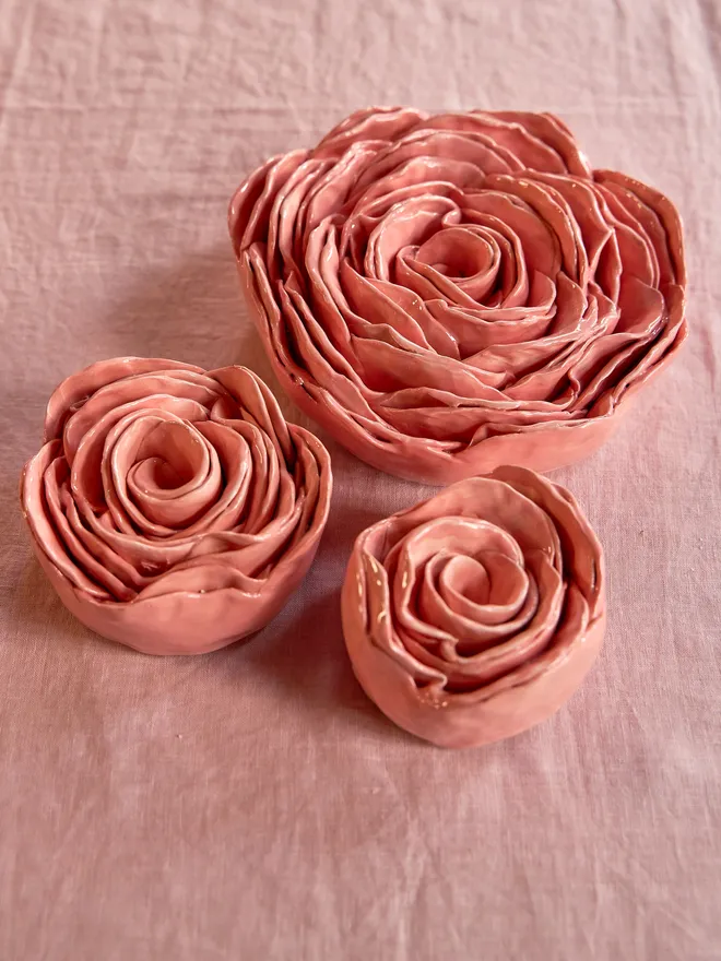 Selection of three pink ceramic roses in small, medium and large size against a pale pink tablecloth