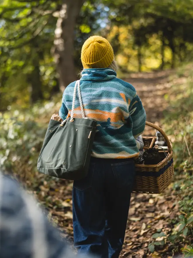 'the henley' canvas picnic bag. a woman with a picnic basket photographed from behind, with a canvas picnic bag hanging over her shoulder.