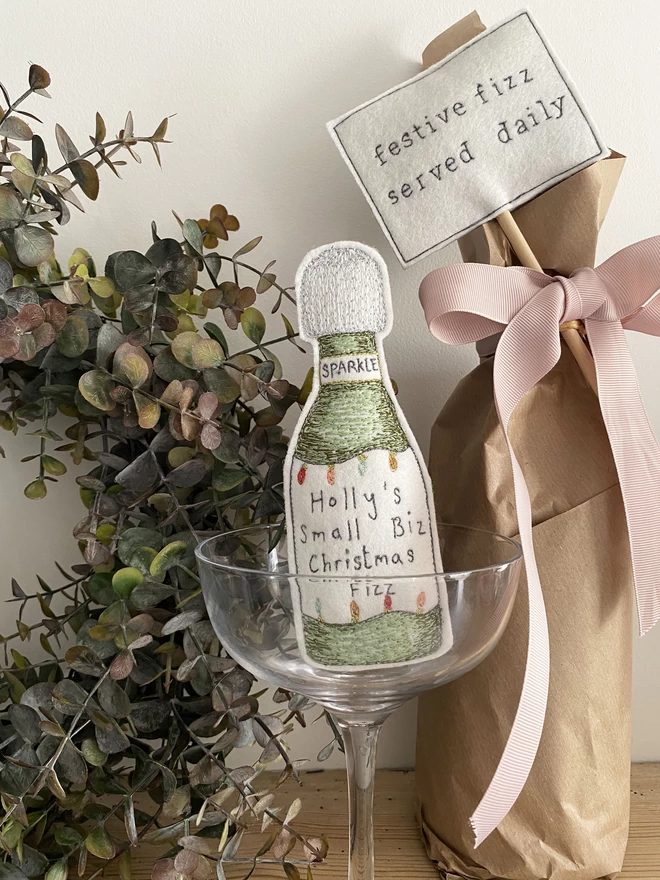 A Little more Christmas Fizz Bottle in glass with wreath and wrapped bottle with festive fizz sign