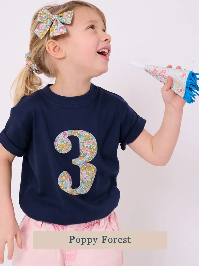 A birthday girl wearing navy  t-shirt with a number 3 cut from liberty floral poppy forest print on the front