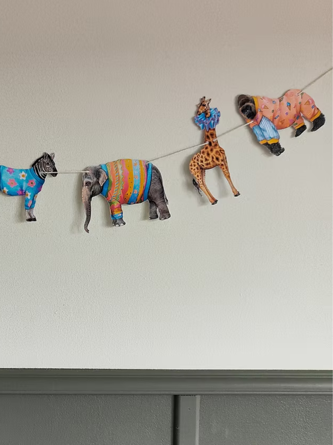 safari animals paper garland. bunting featuring illustrated animals in party outfits hung on a wall.