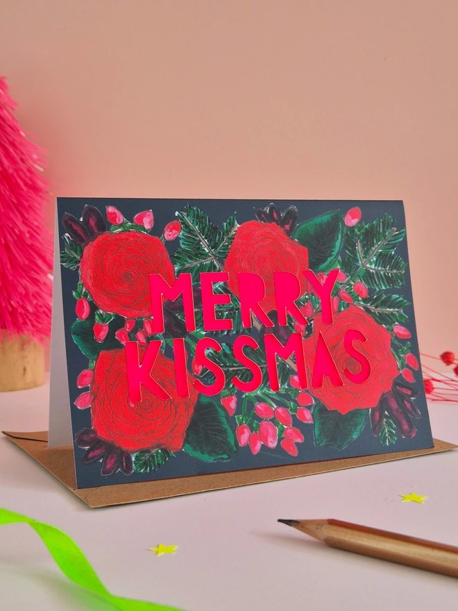 Rose Print Christmas Card with Merry Kissmas in paper cut text and a neon pink paper liner 